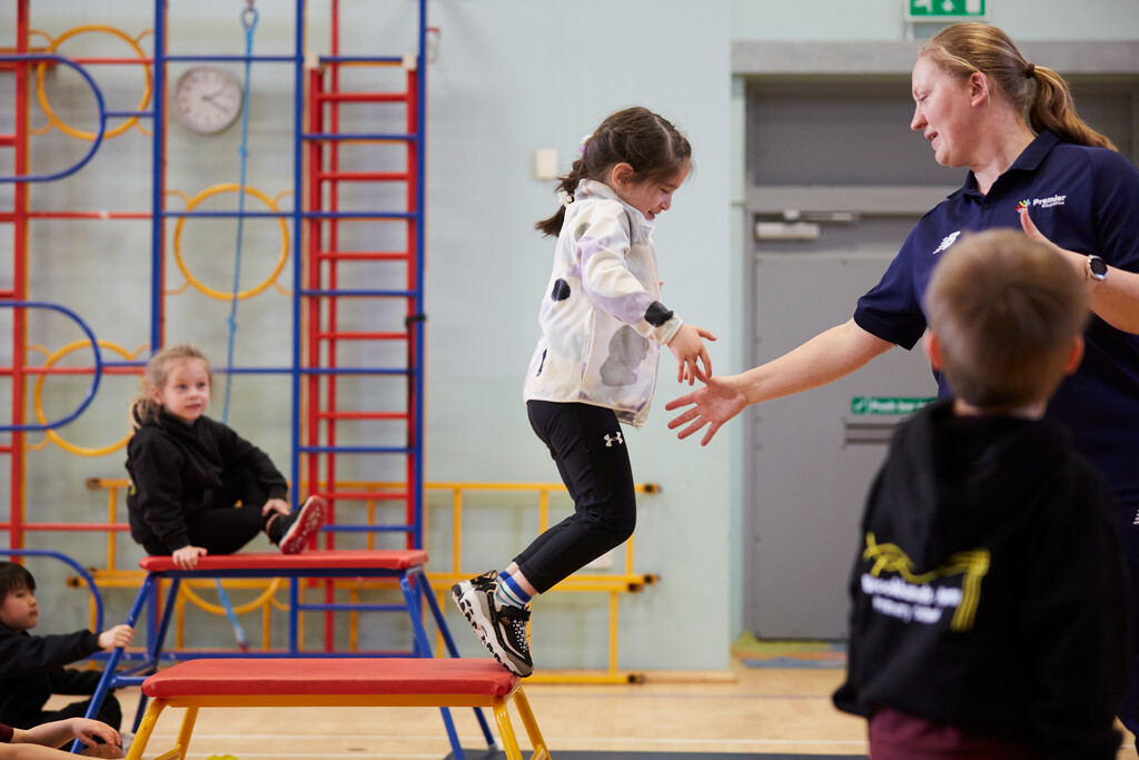 Premier Education coach helping a child off a gymnastics podium during an activity class 